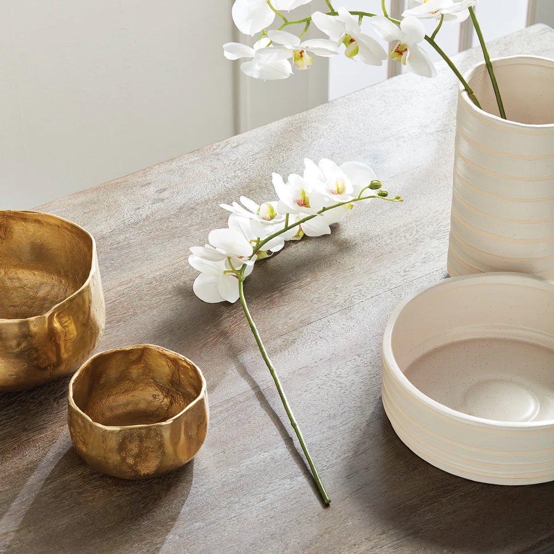 Two gold bowls and a white vase with flowers on a wooden surface