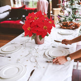 Dining table set with red poinsettias, white plates, and silverware in a festive setting.