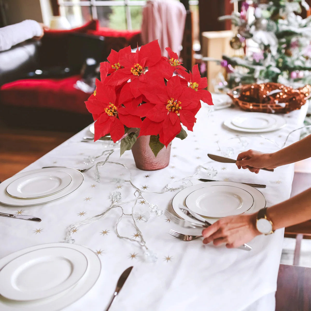 Dining table set with red poinsettias, white plates, and silverware in a festive setting.