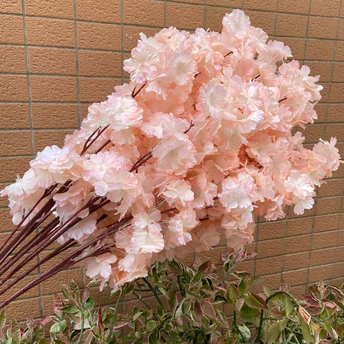 Bouquet of pink artificial cherry blossom flowers against a beige tiled wall