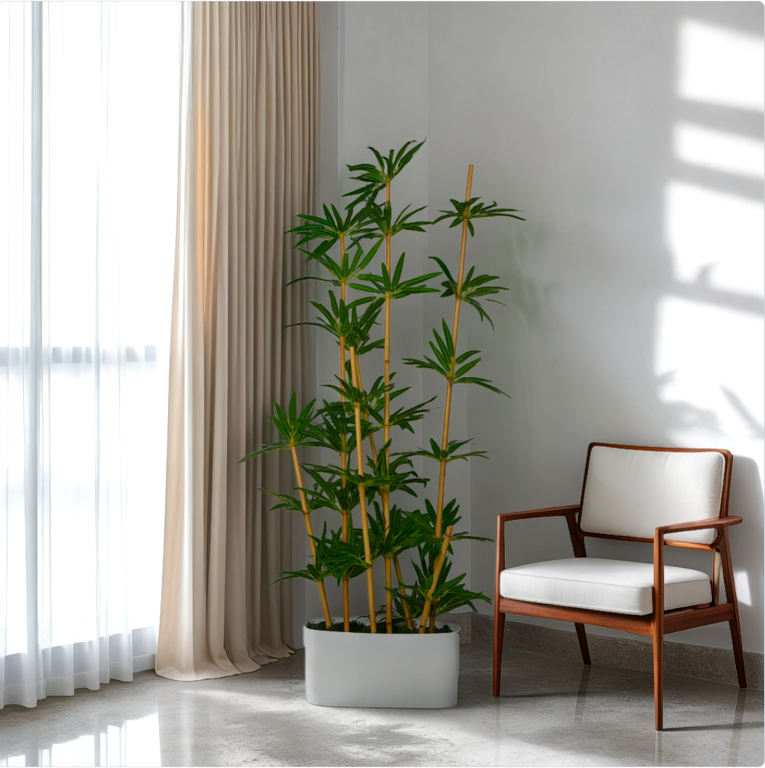 A 5 ft artificial bamboo plant arrangement in a living room setting, featuring natural green leaves, placed in a white pot on the floor next to a white chair with a wooden frame.