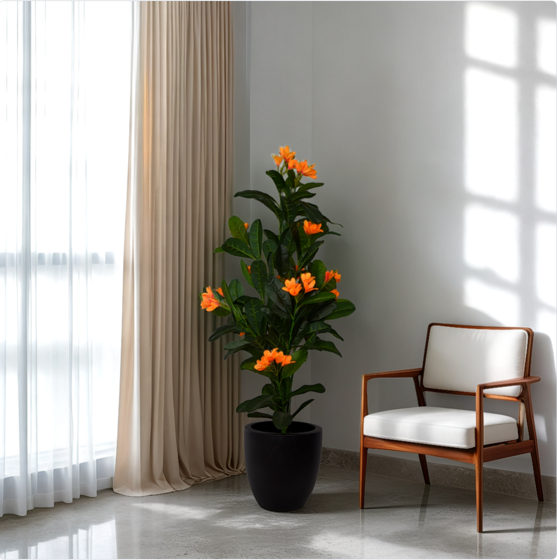 An artificial chicacha flower plant with green leaves and orange flowers in a black pot, placed in a room corner next to a white chair with a window in the background.