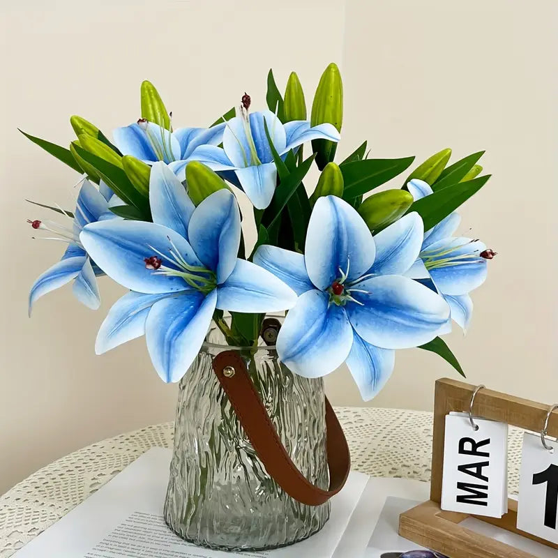 Clear glass vase with brown handle holding blue flowers on a white surface with a beige background