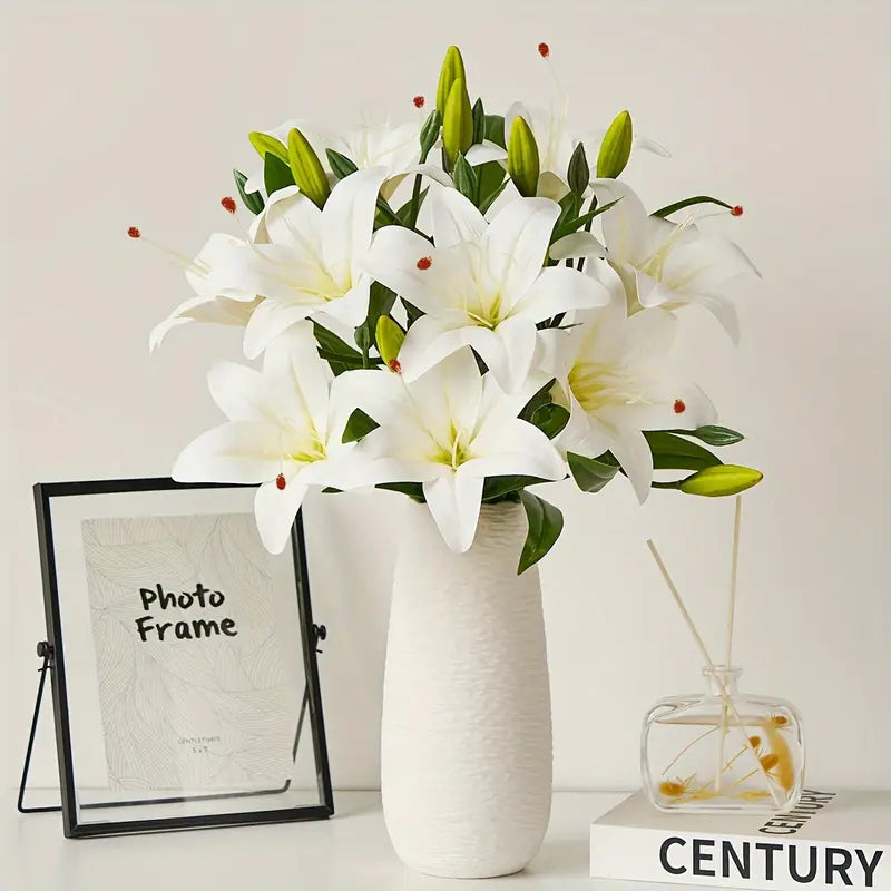 White lilies in a vase on a table with a photo frame and small glass container in the background.
