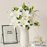 White lilies in a vase on a table with a photo frame and small glass container in the background.