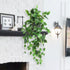 Artificial green vine hanging above a white brick fireplace with decorative items.
